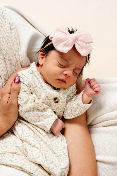 Newborn baby wearing a floral outfit and pink headband, lying on a white surface.