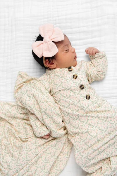 Newborn baby wearing a floral outfit and pink headband on a white background