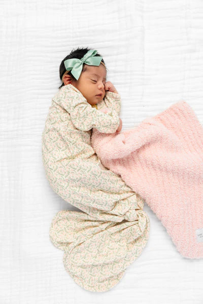 Newborn baby wrapped in a textured blanket with a pink blanket and headband on a white background