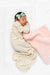 Newborn baby wrapped in a textured blanket with a pink blanket and headband on a white background