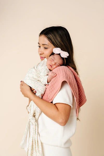 Woman holding a baby wrapped in a pink blanket against a beige background