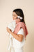 Woman holding a baby wrapped in a pink blanket against a beige background