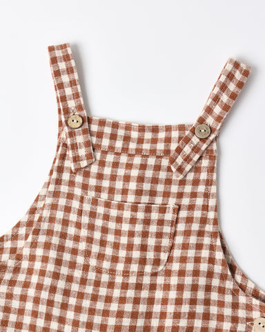Brown and cream gingham check pinafore overalls with adjustable straps and wooden buttons, shown on a clean white background.
