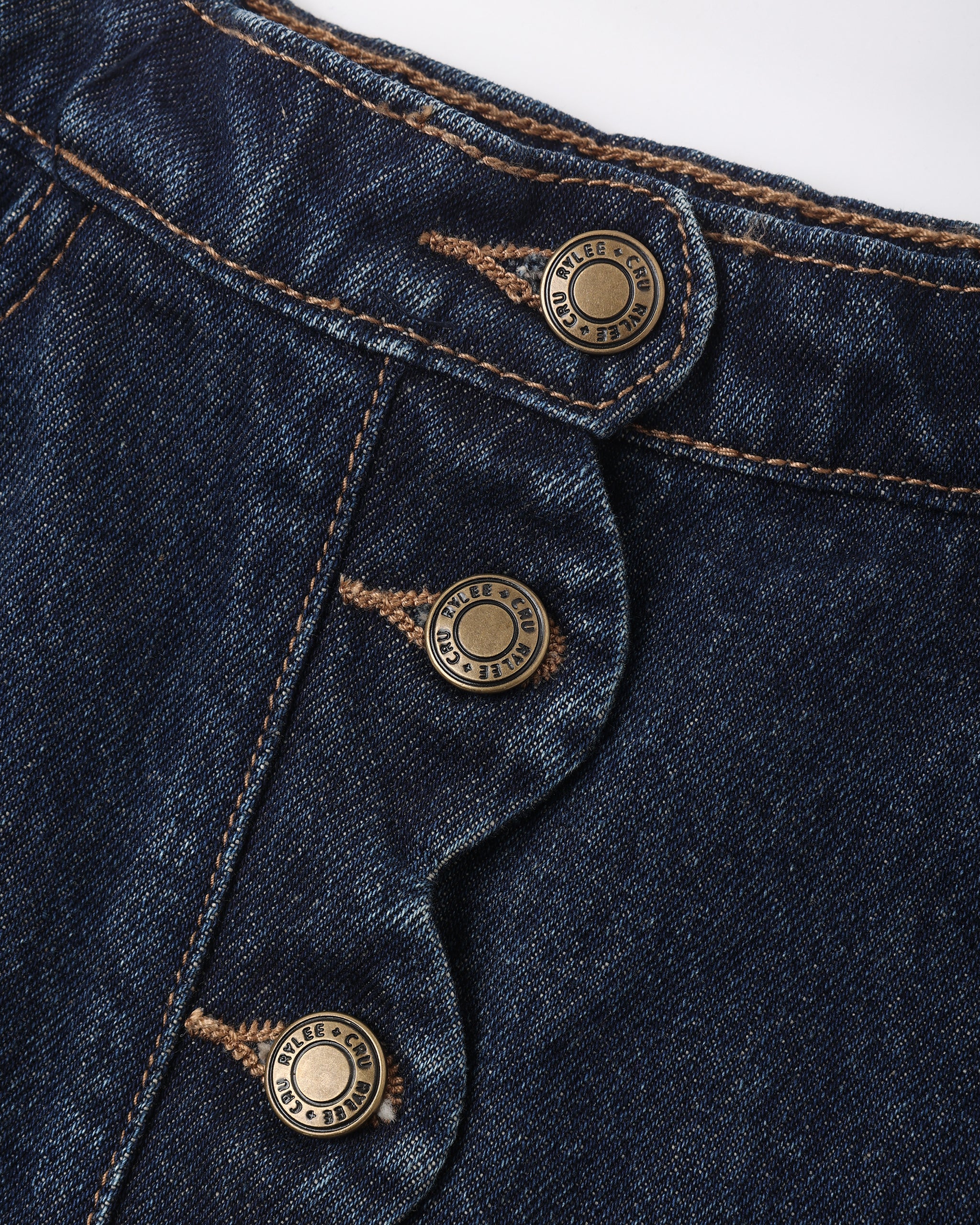 Close-up of dark indigo denim fabric with three brass buttons and contrast tan stitching, showing the button details and denim texture.