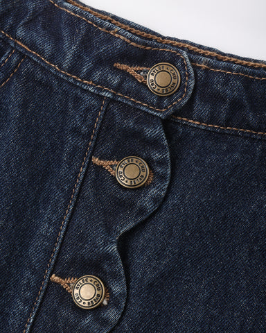Close-up of dark indigo denim fabric with three brass buttons and contrast tan stitching, showing the button details and denim texture.