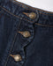Close-up of dark indigo denim fabric with three brass buttons and contrast tan stitching, showing the button details and denim texture.