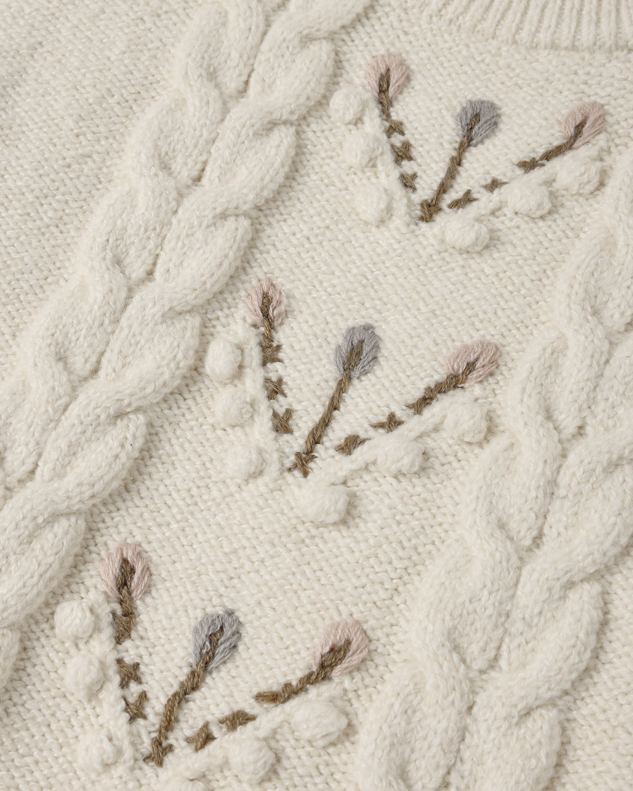 A close up of anatural colored sweater with a floral design down the center 
