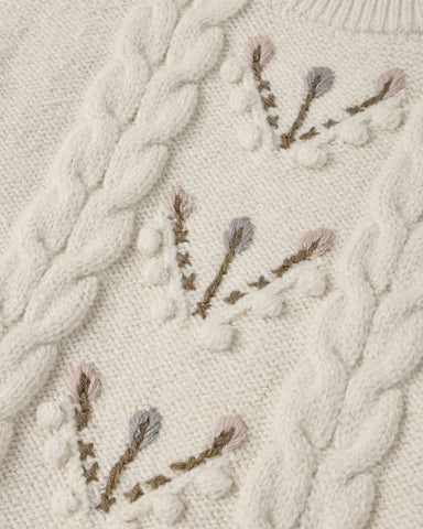 A close up of anatural colored sweater with a floral design down the center 