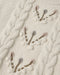 A close up of anatural colored sweater with a floral design down the center 