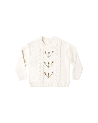A natural colored sweater with a floral design down the center shown on a white background
