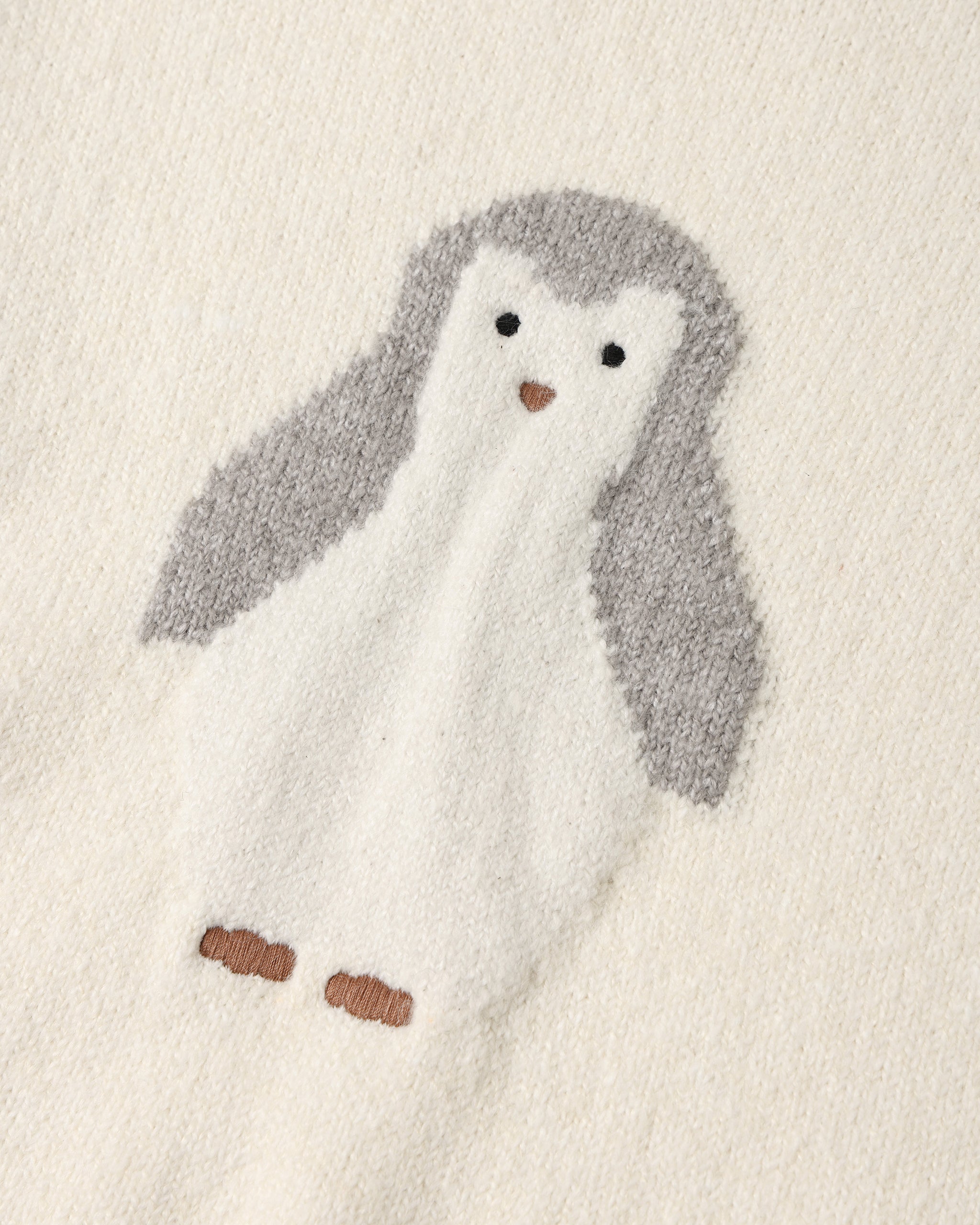 A close-up of a soft knit fabric featuring a penguin motif in white and gray with small brown accents.