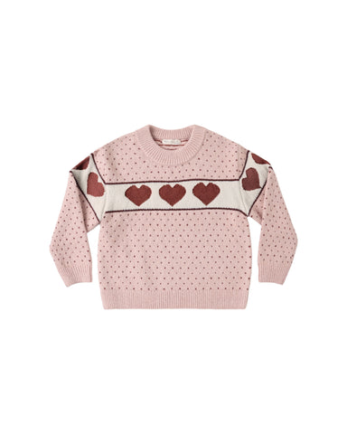 A blush colored sweater with red hearts on a white stripe shown on a white background.
