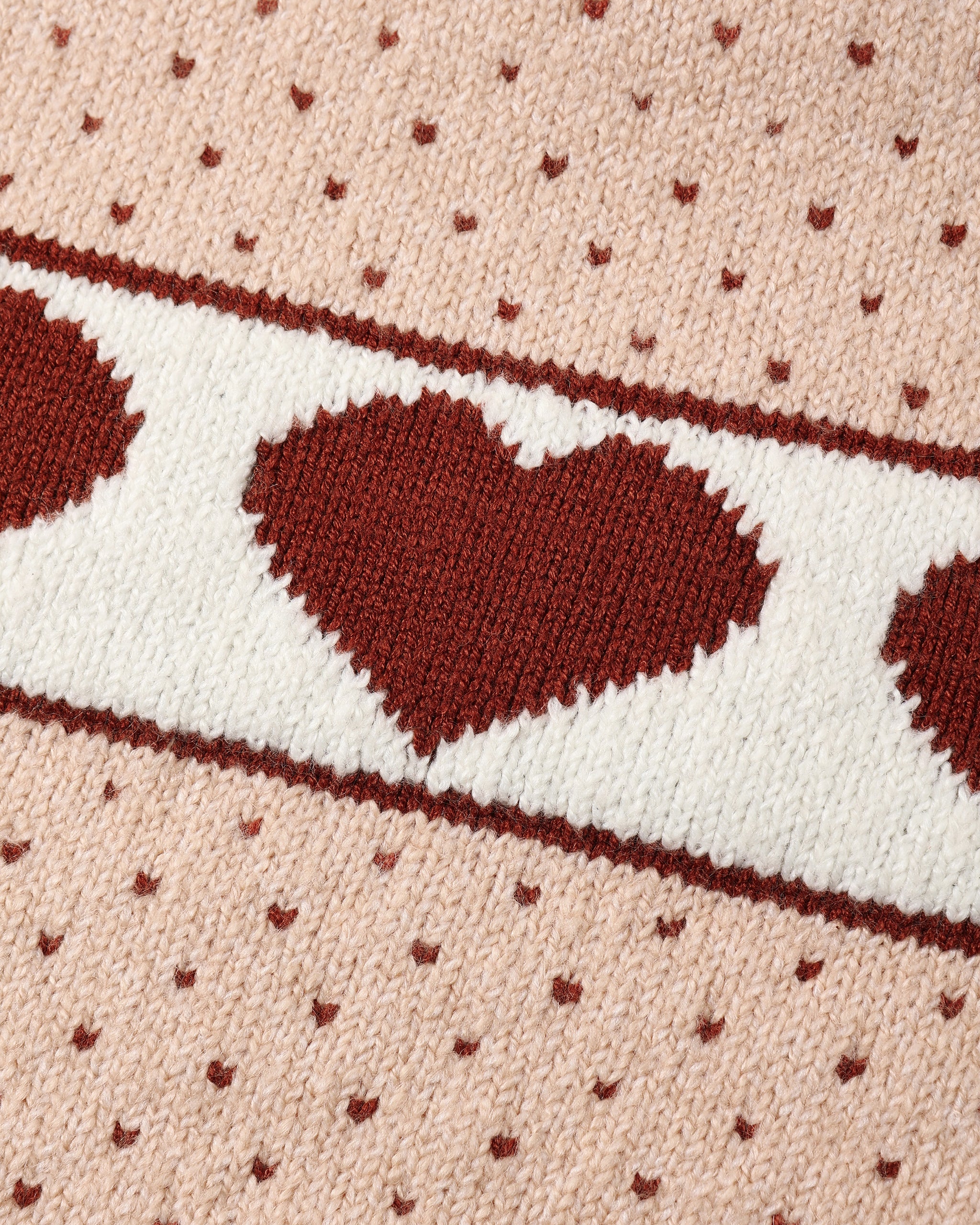 Close-up of a knitted textile pattern featuring large dark red hearts and small heart motifs on a light pink background, with a horizontal cream band across the center.