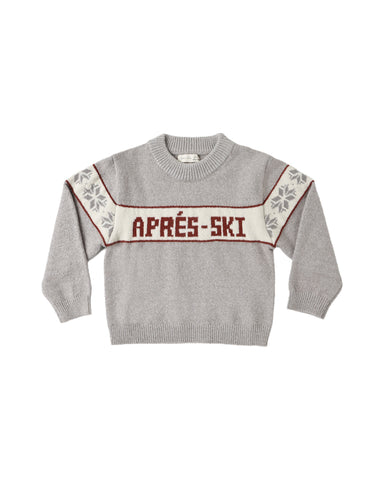 A light gray knit crewneck sweater with a cream horizontal chest stripe reading 'APRÉS-SKI' in dark red letters, bordered by thin red lines. The sleeves have cream panels with gray floral motifs and red trim.