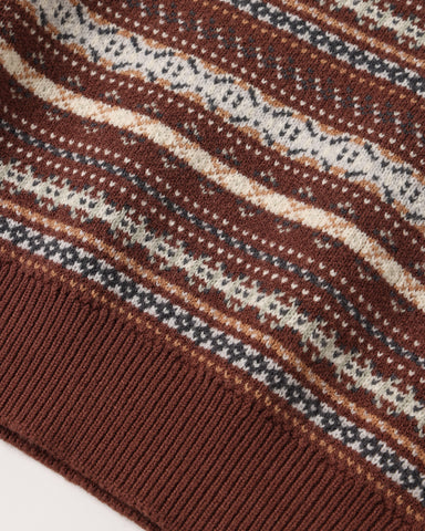 Close-up of a knit sweater corner showing a brown ribbed cuff and a Fair Isle style pattern with horizontal stripes in brown, cream, and dark gray.
