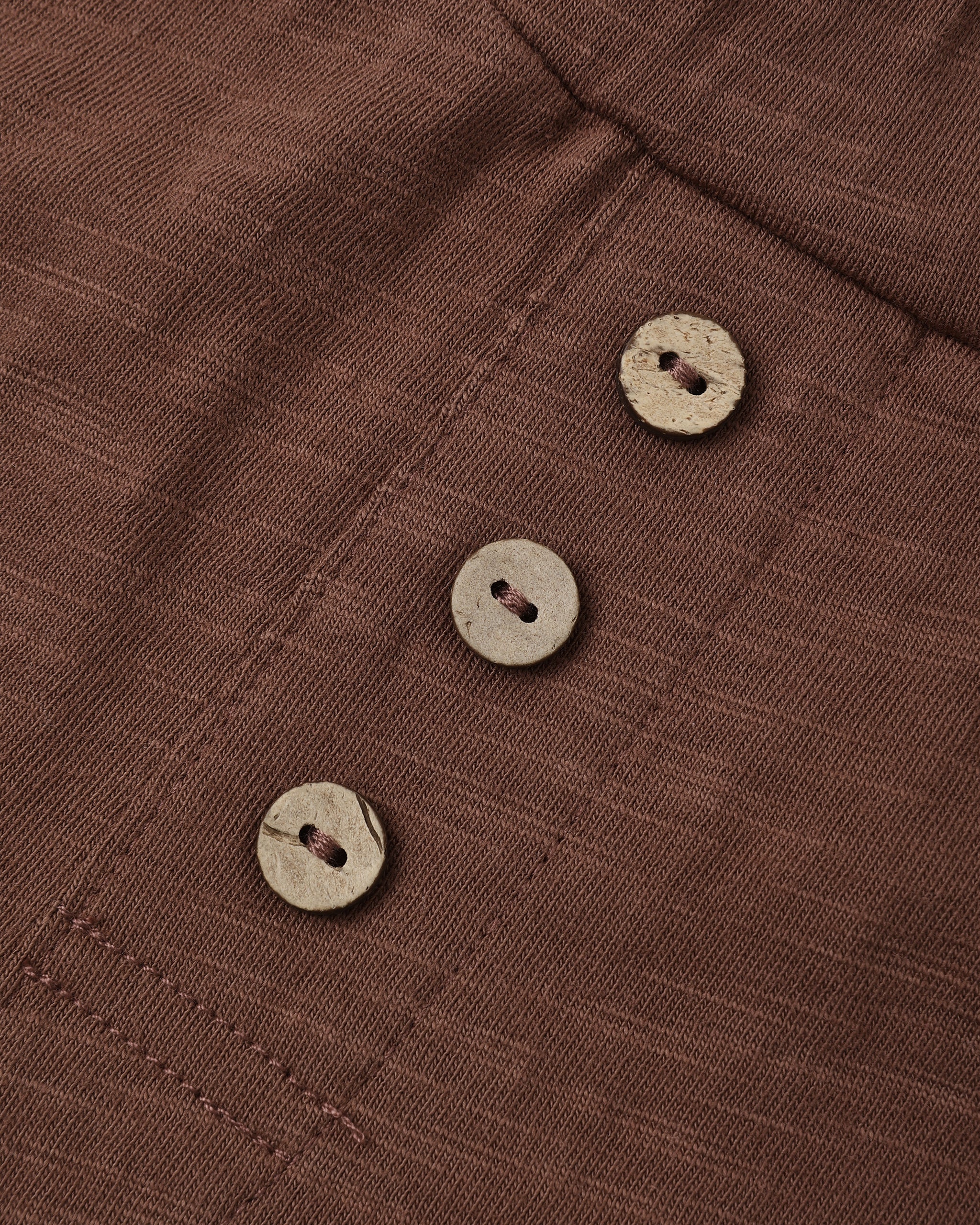 Close-up of a brown textured fabric garment with three round natural wood buttons aligned vertically.