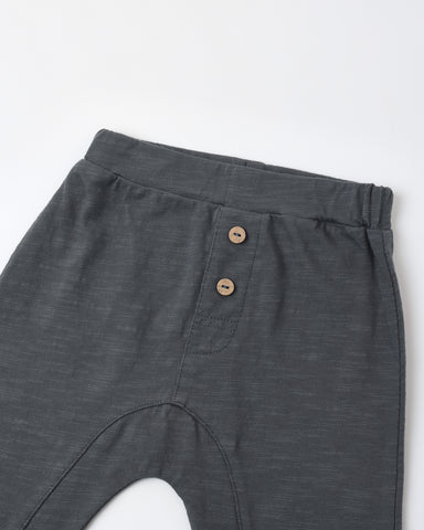 Close-up of dark gray heathered pants showing the waistband, side pocket with two brown buttons, and part of the leg on a white background.