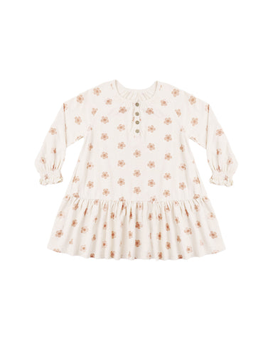 A long sleeve swing dress featuring a gathered lower tier, cinched wrists, and coconut button snaps down the front shown on a white background
