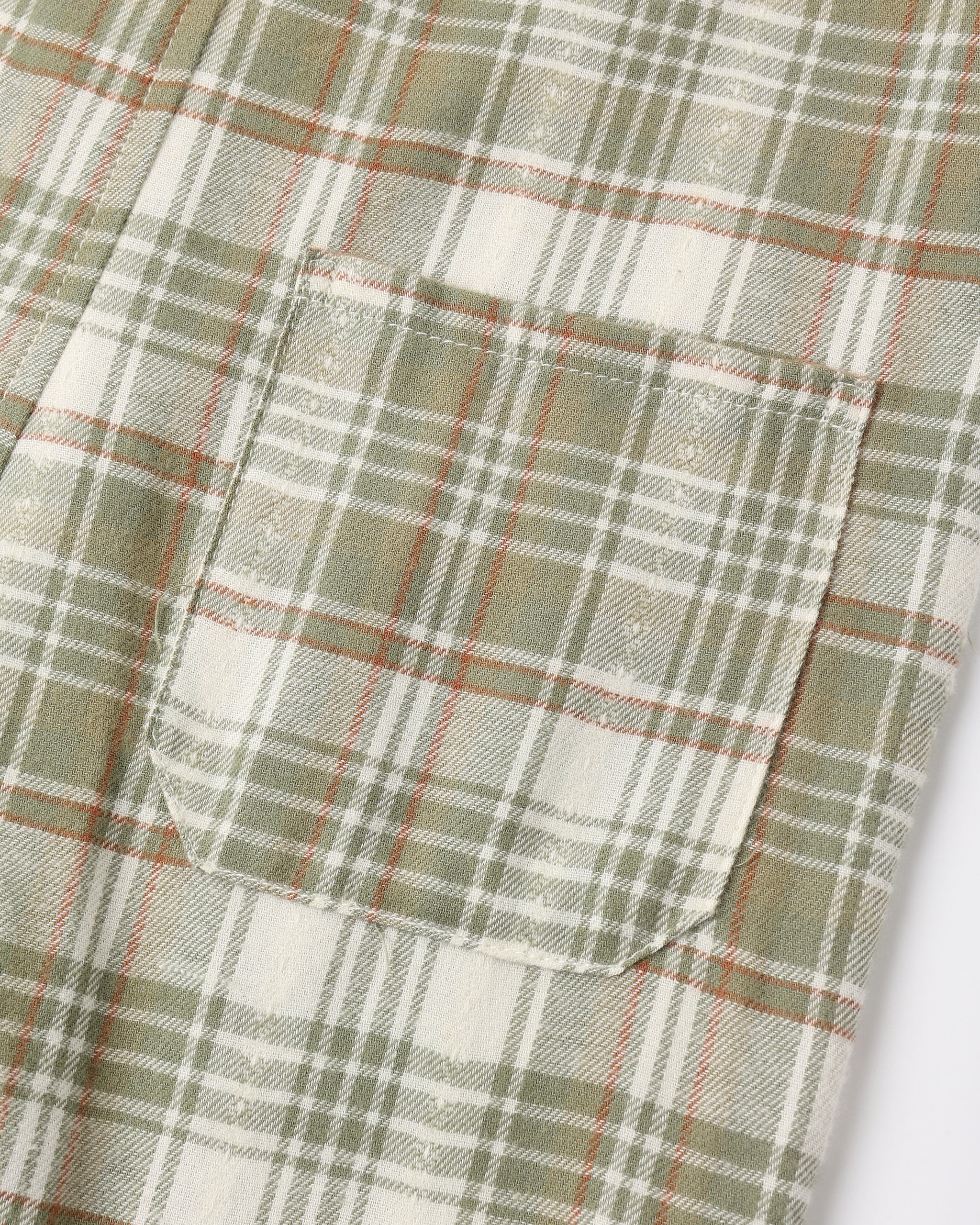 Close-up of a plaid fabric garment showing a pocket and pattern details in muted green, cream, and thin orange-red lines.