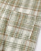 Close-up of a plaid fabric garment showing a pocket and pattern details in muted green, cream, and thin orange-red lines.