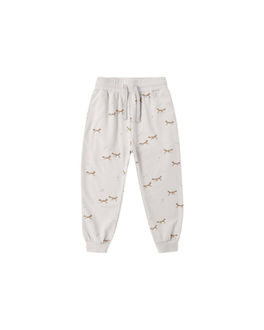 A pair of light beige jogger pants with an all-over print of small brown foxes and tiny dandolions, featuring an elastic waistband with a drawstring and elastic cuffs.