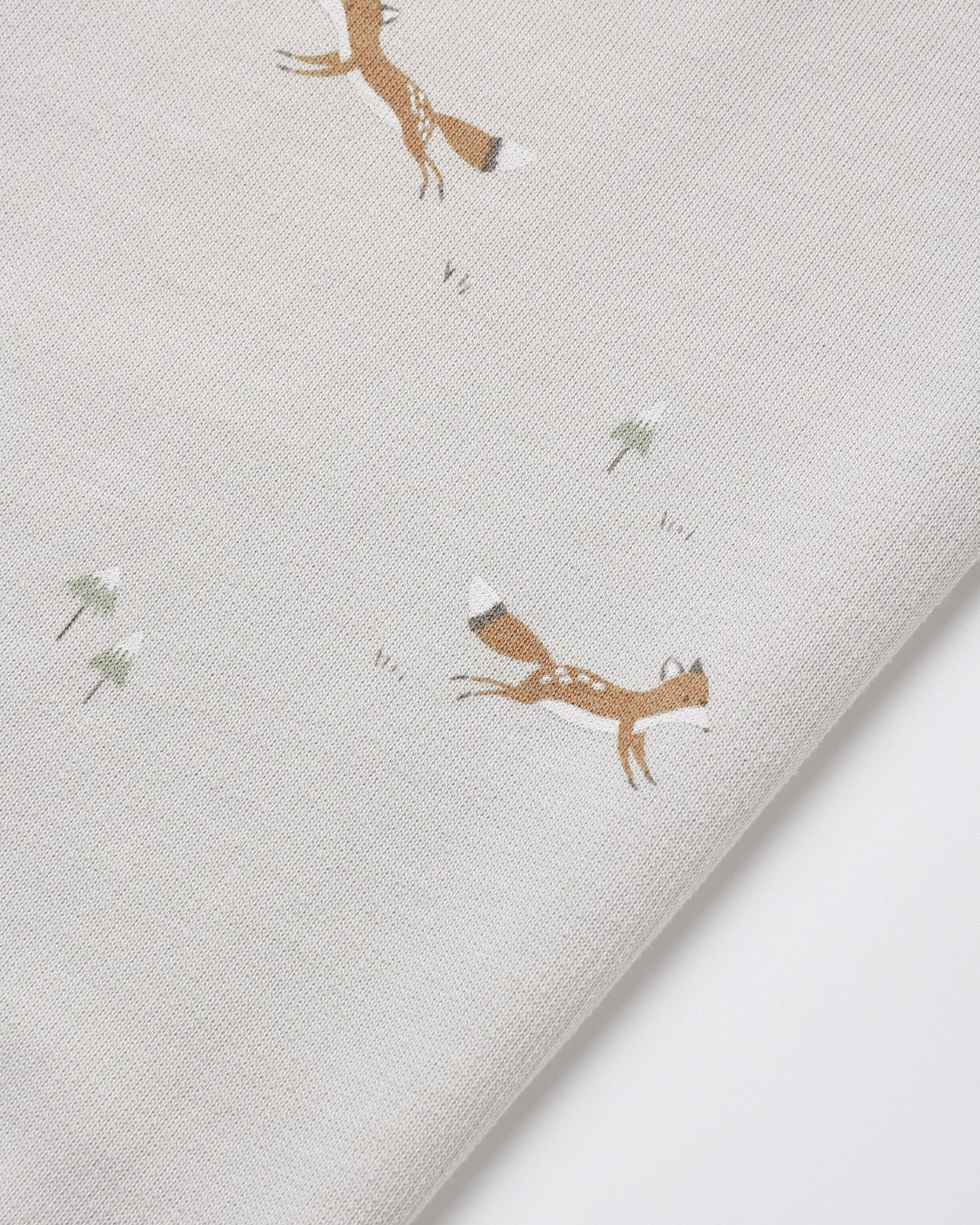 A close-up of a light gray fabric with a printed pattern of brown foxes and small white flowers, folded diagonally.