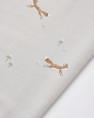 A close-up of a light gray fabric with a printed pattern of brown foxes and small white flowers, folded diagonally.