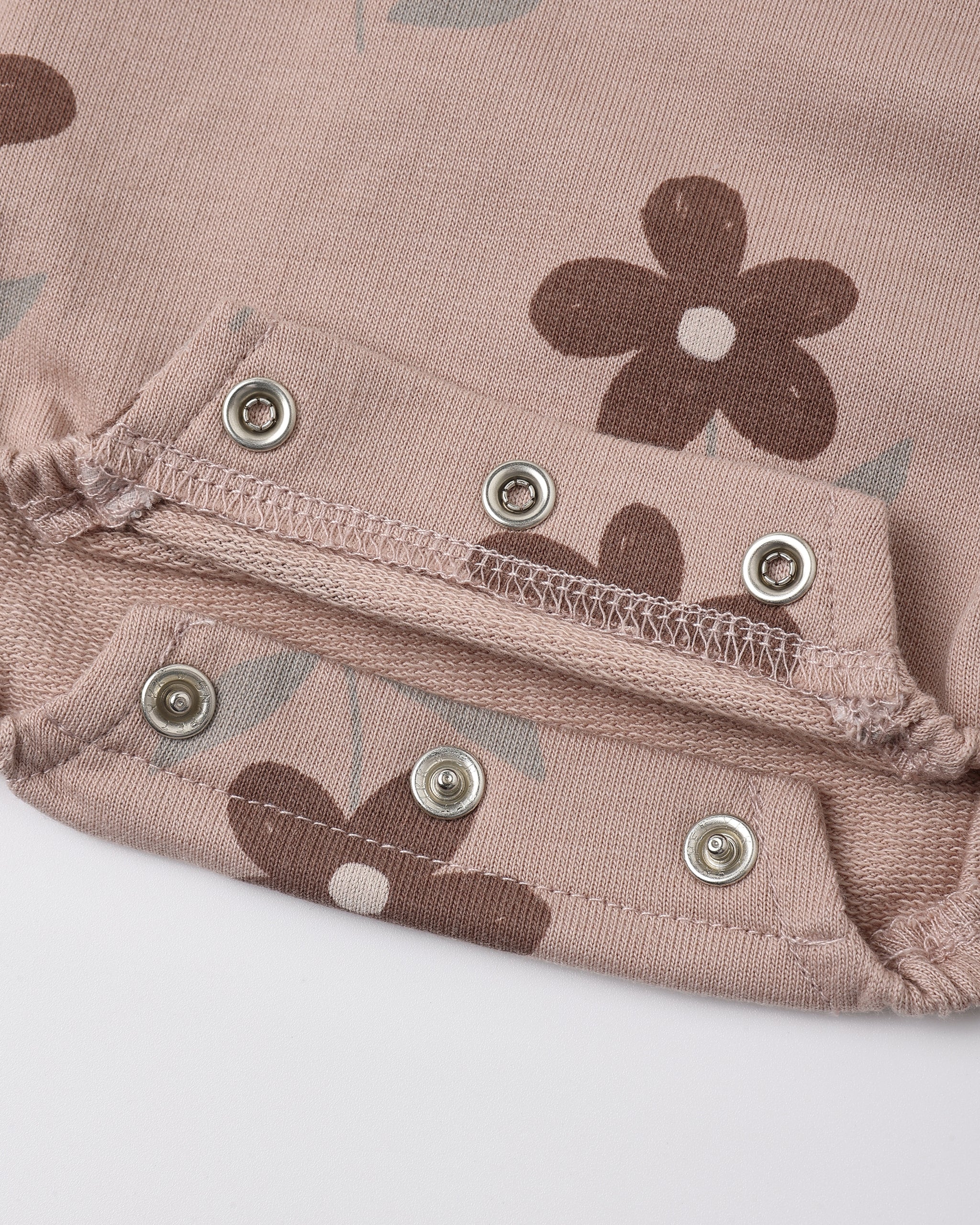 Close-up of a dusty pink fabric garment with a brown floral print and silver metal snap buttons.