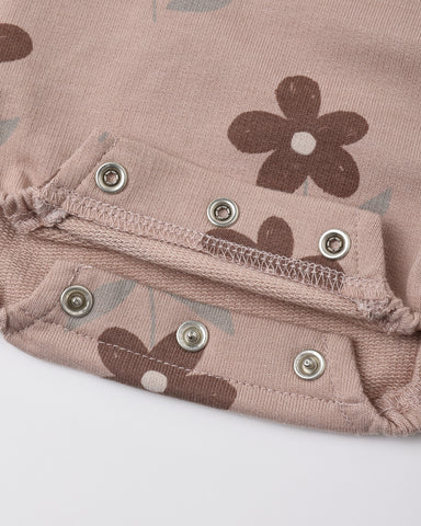 Close-up of a dusty pink fabric garment with a brown floral print and silver metal snap buttons.