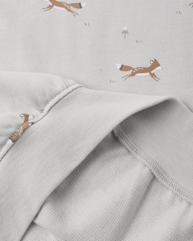 Close-up of a light gray fabric garment with a soft fold, showing a subtle print of brown foxes and small white dandelions on the fabric.