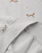 Close-up of a light gray fabric garment with a soft fold, showing a subtle print of brown foxes and small white dandelions on the fabric.