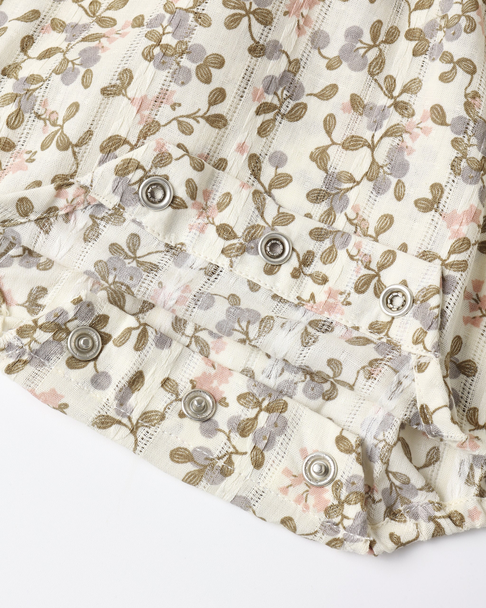 An close up of an ivory colored romper with a small floral pattern with snap closure for easy diaper change.