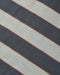 A close-up of a striped textile pattern featuring diagonal bands of dark charcoal gray, light beige, and thin rust-red lines.