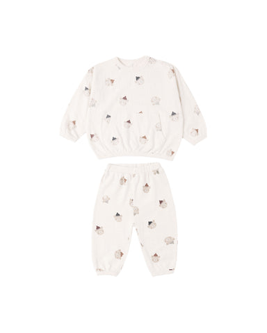 A two-piece baby set featuring a long-sleeve top and matching pants in an off-white/cream color, both printed with a small, scattered pattern of teddy bears in soft brown and gray tones.