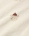 Close-up of a cream-colored fabric with a small embroidered teddy bear face wearing a brown knit hat.