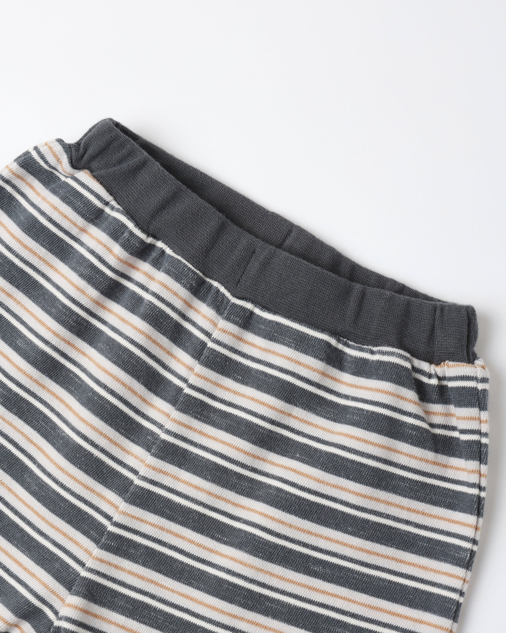 Close-up of striped lounge pants with a dark gray elastic waistband, featuring horizontal stripes in dark gray, beige, and white on a light gray background.