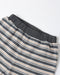 Close-up of striped lounge pants with a dark gray elastic waistband, featuring horizontal stripes in dark gray, beige, and white on a light gray background.