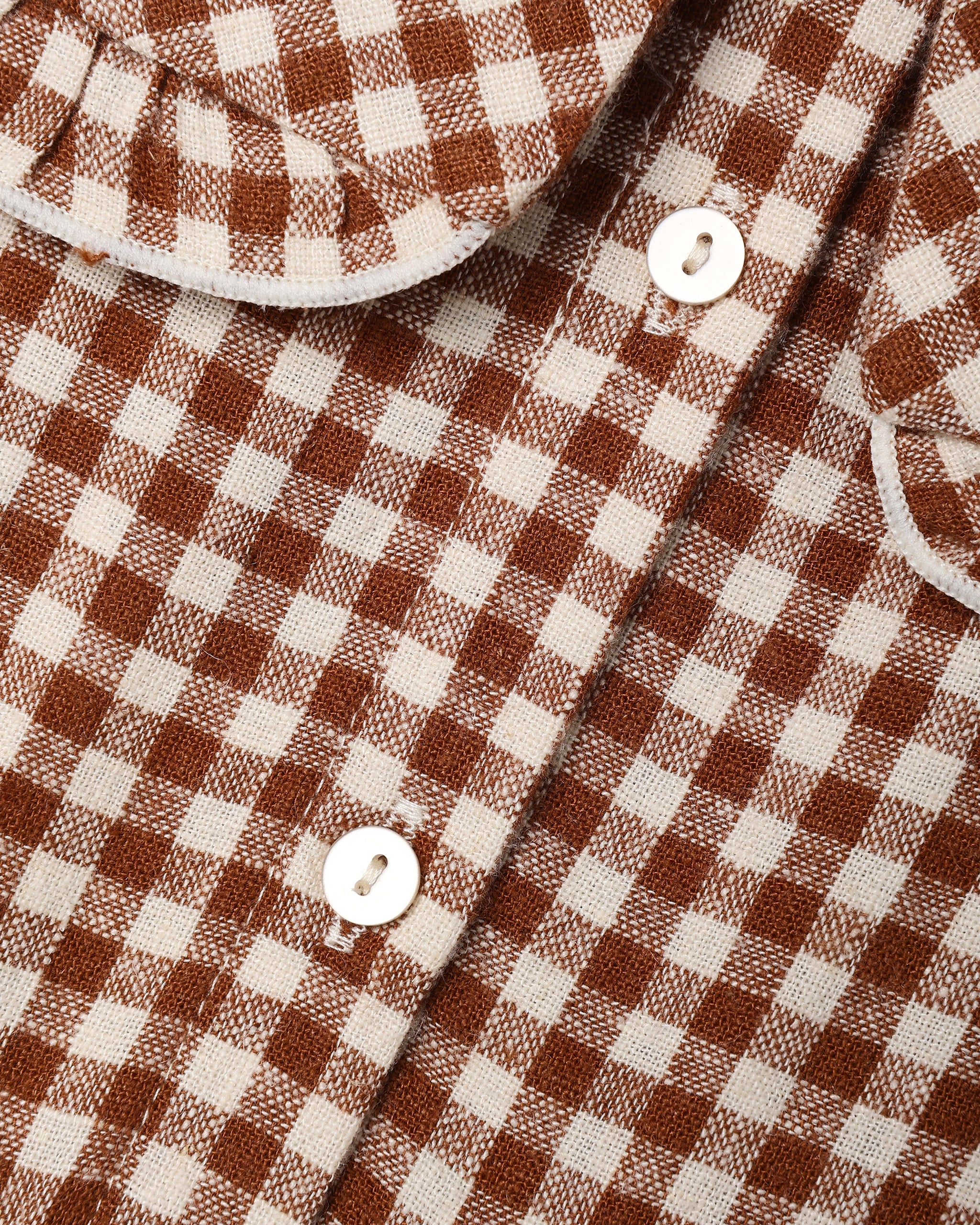 A close up of a brown and white gingham check pattern fabric, featuring buttons in the back
