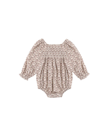 A baby long-sleeve romper with a dense beige and brown floral pattern, featuring a smocked bodice and ruffled sleeves, shown flat on a white background.