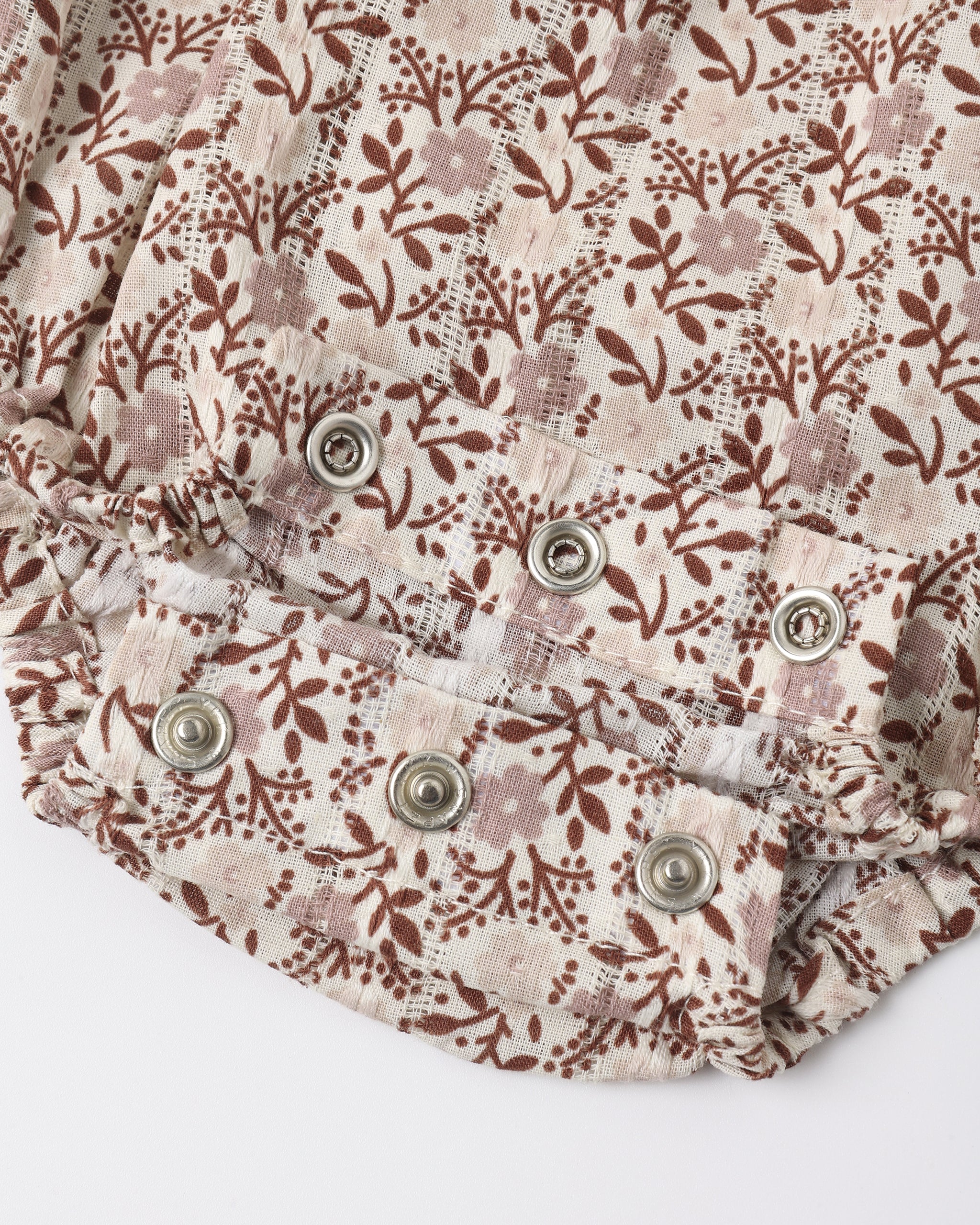 Close-up of a floral-patterned fabric garment, likely a skirt or shorts, featuring a brown and dusty pink floral print on a cream background with decorative metal snap buttons.