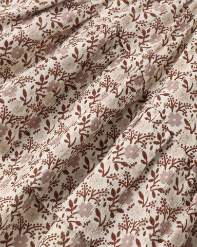 A close-up of a draped fabric with an all-over floral and leafy pattern in brown and dusty mauve on a warm off-white background.