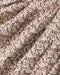 A close-up of a draped fabric with an all-over floral and leafy pattern in brown and dusty mauve on a warm off-white background.