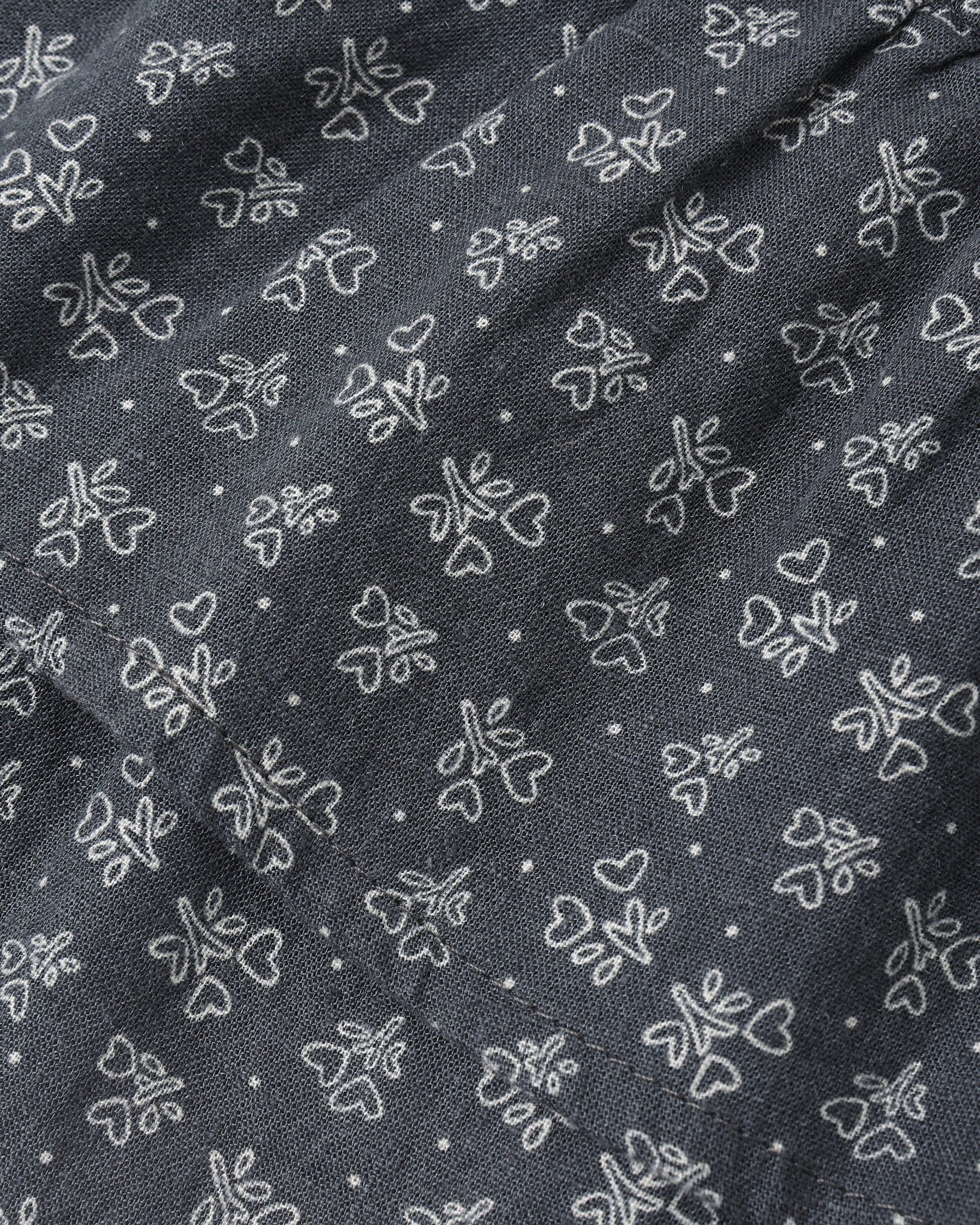 A close-up of dark gray fabric with a repeating white embroidered pattern of small flowers, hearts, and dots.