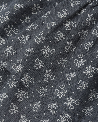 A close-up of dark gray fabric with a repeating white embroidered pattern of small flowers, hearts, and dots.