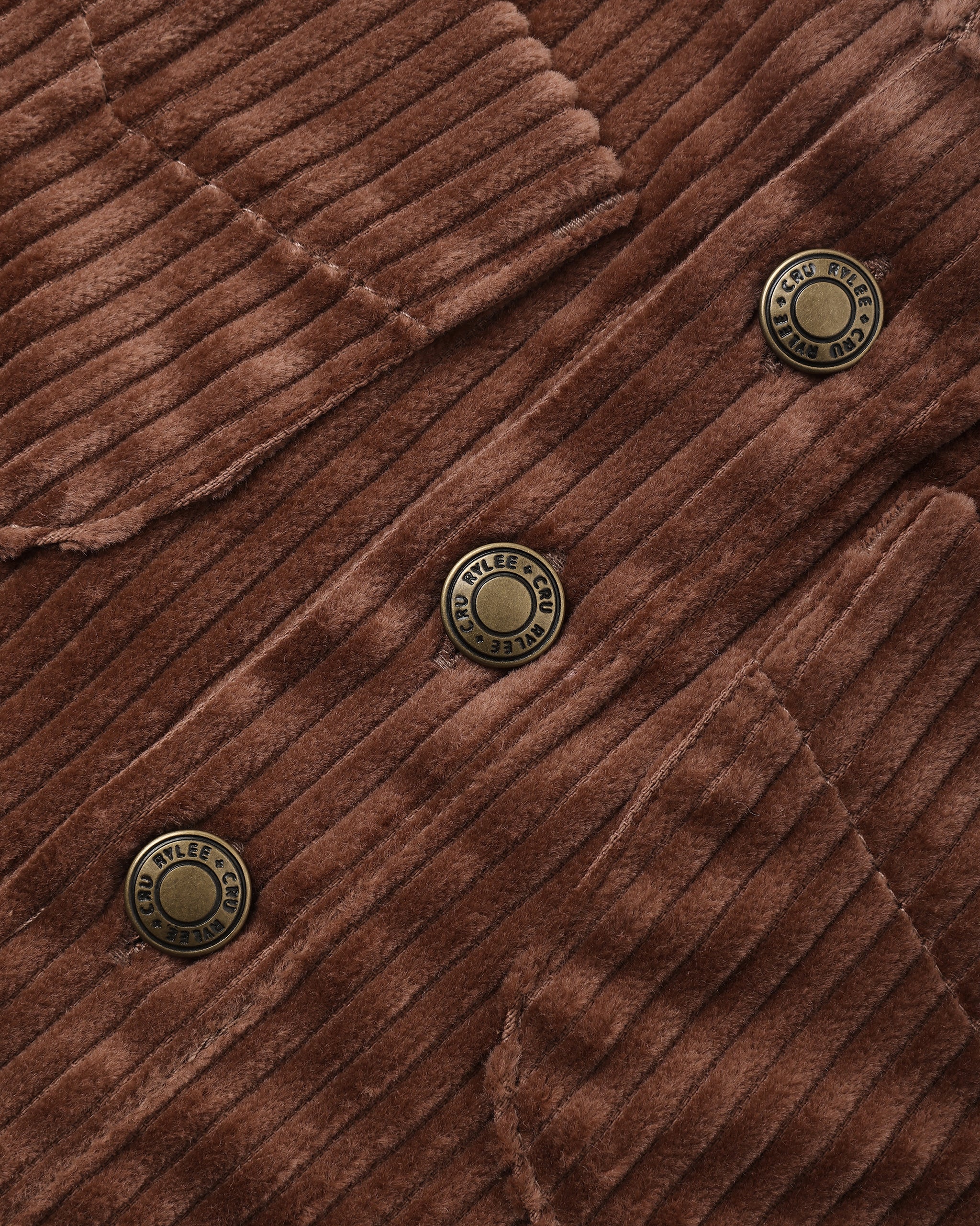 Close-up of a brown corduroy fabric with three round bronze buttons, showing the ribbed texture and stitched details.