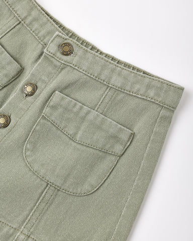 Close-up of a light sage green corduroy garment, showing a buttoned pocket and metal buttons on a white background.
