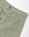 Close-up of a light sage green corduroy garment, showing a buttoned pocket and metal buttons on a white background.