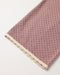 A close-up of a dusty pink textured fabric item, likely a blanket or scarf, featuring a scalloped cream border on a plain white background.
