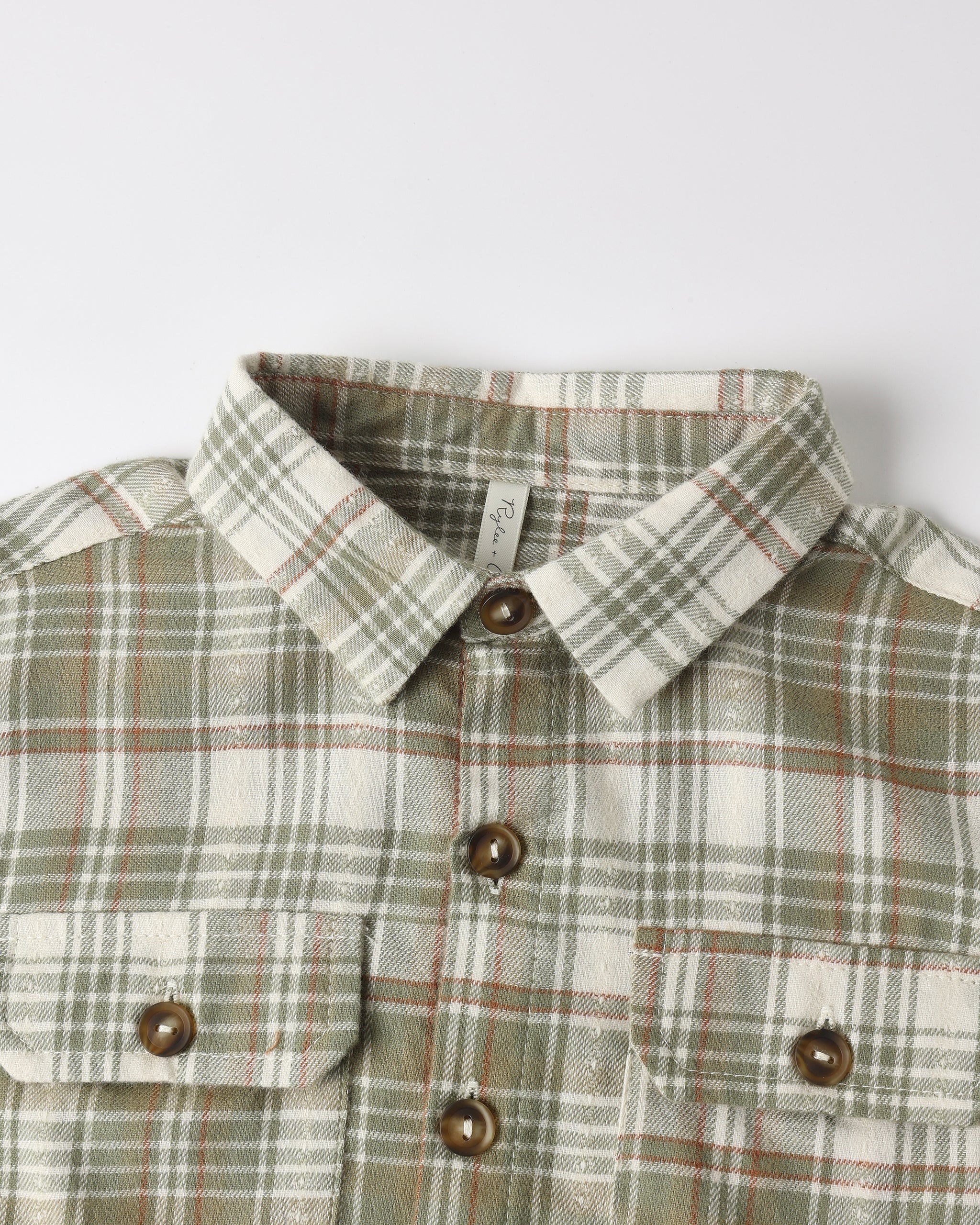 A close-up of a plaid button-down shirt with a pointed collar, brown buttons, and two chest pockets on a light gray background.