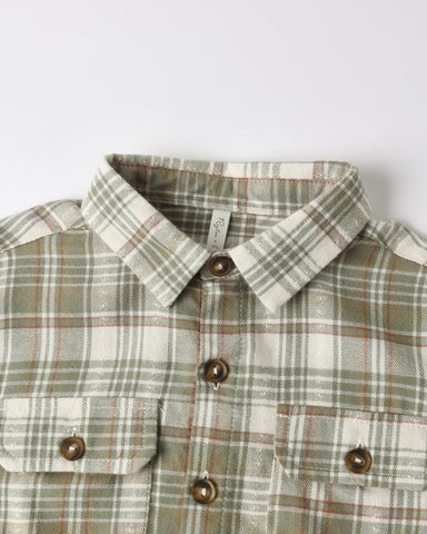 A close-up of a plaid button-down shirt with a pointed collar, brown buttons, and two chest pockets on a light gray background.